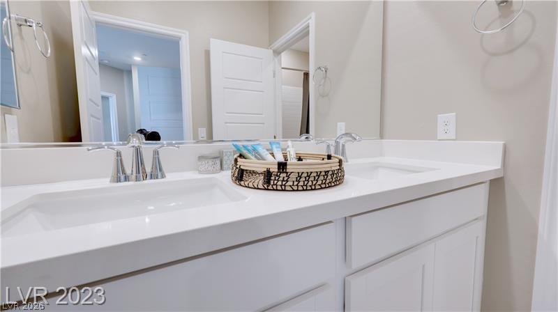 Bathroom vanity with two sinks, chrome faucets, white cabinets, and a basket of toiletries.