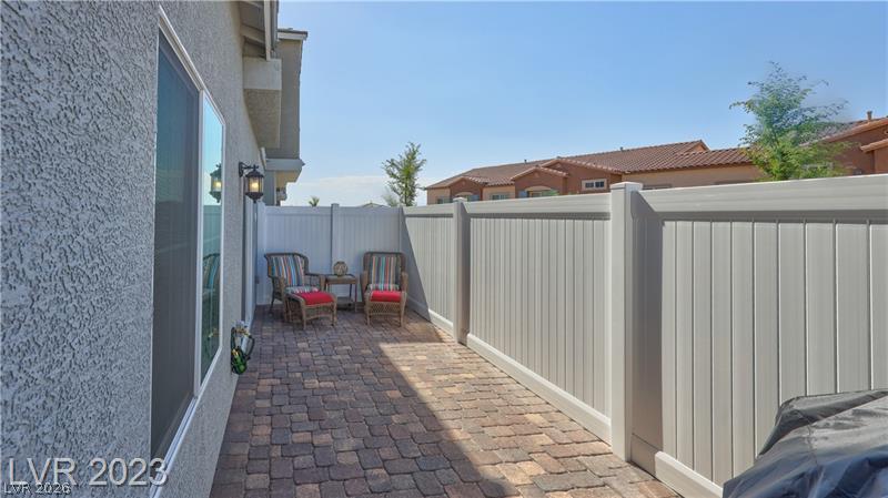 Fenced paver patio beside the home, furnished with two red-cushioned chairs.