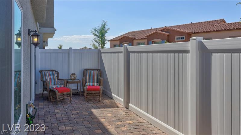 Paved patio with two colorful chairs and a small table inside a white privacy fence.