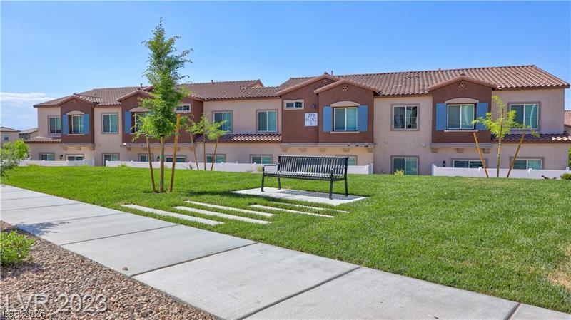 Two-story attached homes with blue shutters, a lawn, young trees, and a black bench.