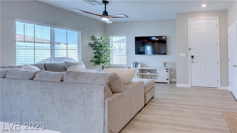 Living room with a light-gray sectional, wall-mounted TV, wide blinded windows, and light wood floors.