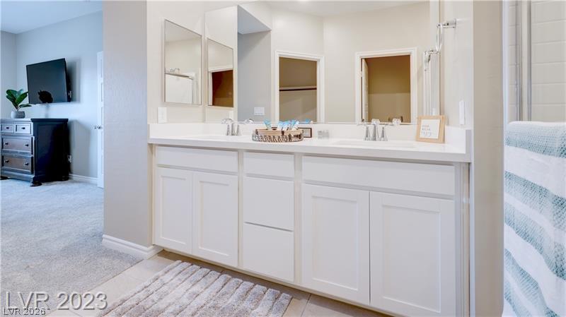Bathroom with a long white double-sink vanity and mirrored cabinets beside a carpeted room.