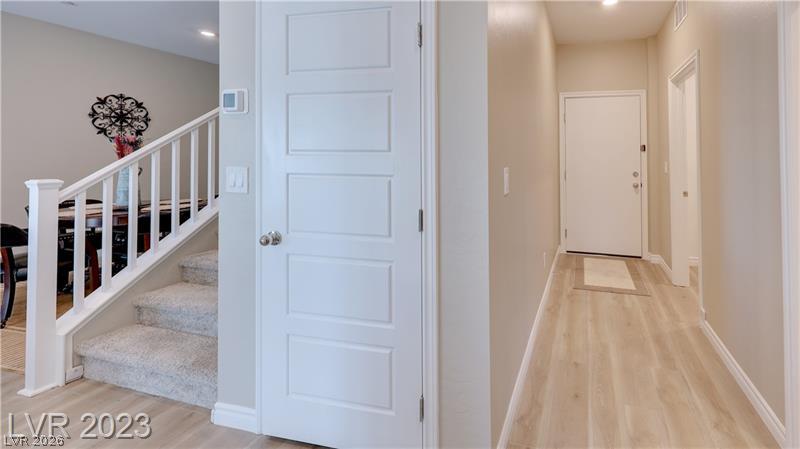 Entryway with a carpeted staircase, white paneled door, and light wood hallway flooring.