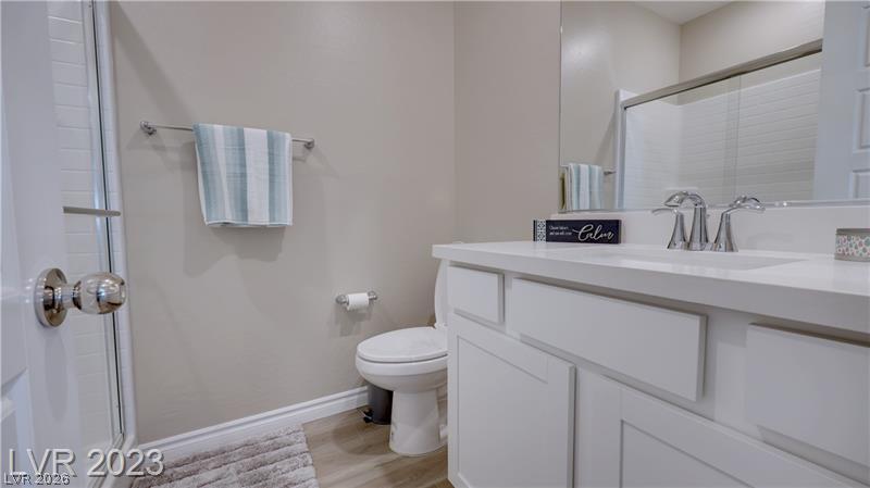 Bathroom with a white paneled vanity, wide mirror, toilet, and glass-enclosed shower.