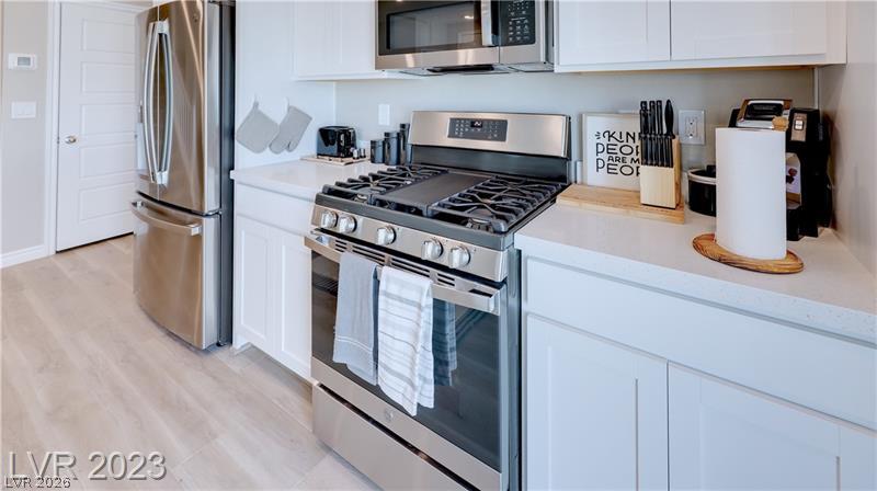 White kitchen with stainless steel appliances, a gas range, and light wood-look flooring.
