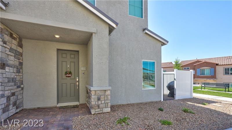 Home entrance with a covered porch, stone accents, gravel landscaping, and a white side-yard gate.