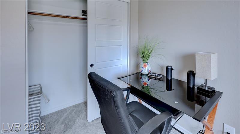 Home office with a black glass-top desk, dark chair, and open closet.