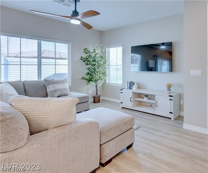 Living room with a beige sectional, wall-mounted TV, large windows, and a ceiling fan.