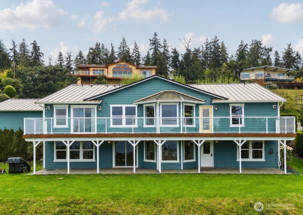 Teal two-story home with a raised wraparound deck and wooded hillside behind it.