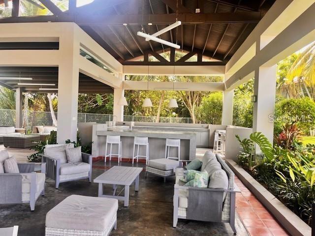 Covered outdoor living area with gray seating, a bar, and tropical landscaping.