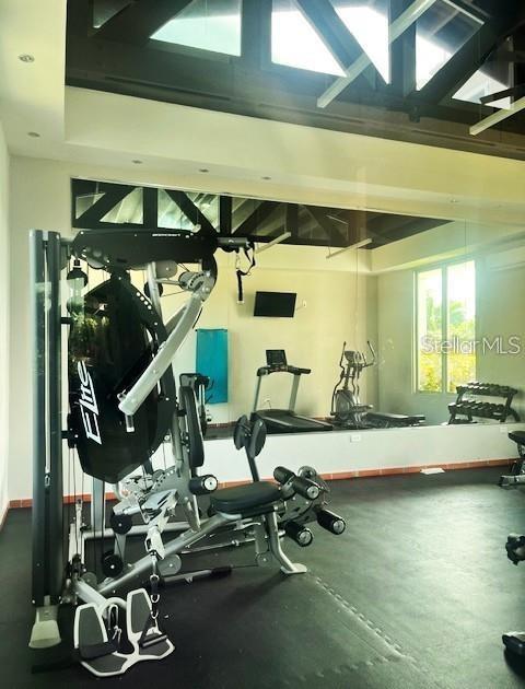Fitness room with strength-training equipment, a treadmill, mirrored wall, and exposed roof framing.