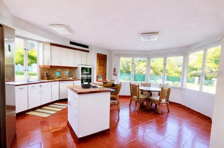 Open kitchen and dining area with a white island, red tile floor, and windows overlooking a pool.