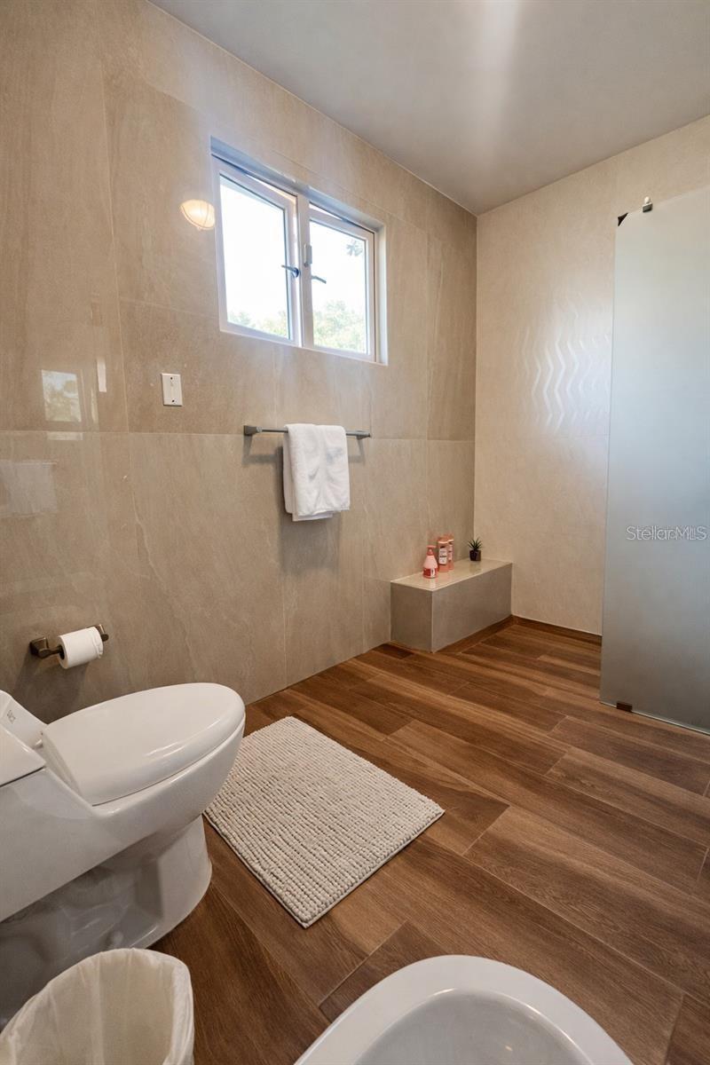 Bathroom with a glass shower enclosure, high window, and wood-look flooring.