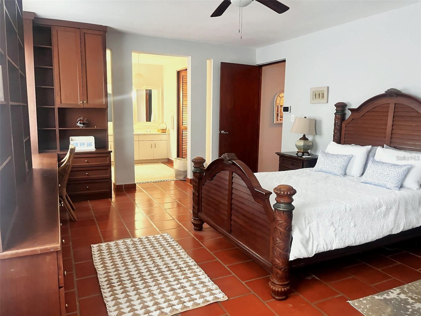 Furnished bedroom with a carved wood bed, terracotta tile floors, and built-in cabinetry.