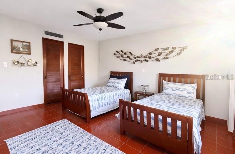 Bedroom with three wooden beds, patterned bedding, terracotta tile, and a ceiling fan.