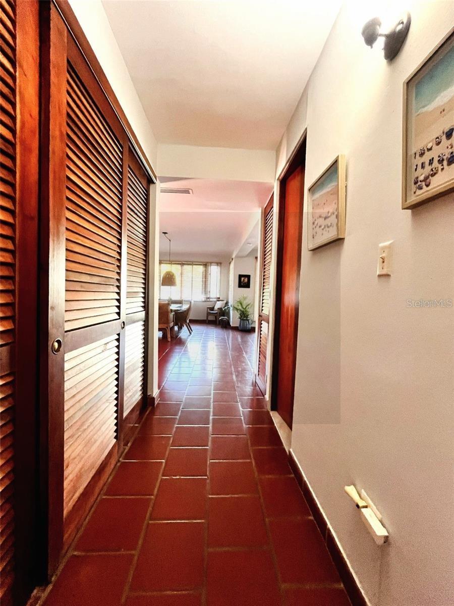 Hallway with terracotta tile, wooden louvered doors, and a dining area at the far end.