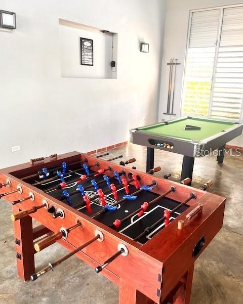 Game room with a wooden foosball table and a green-felt pool table by a louvered window.