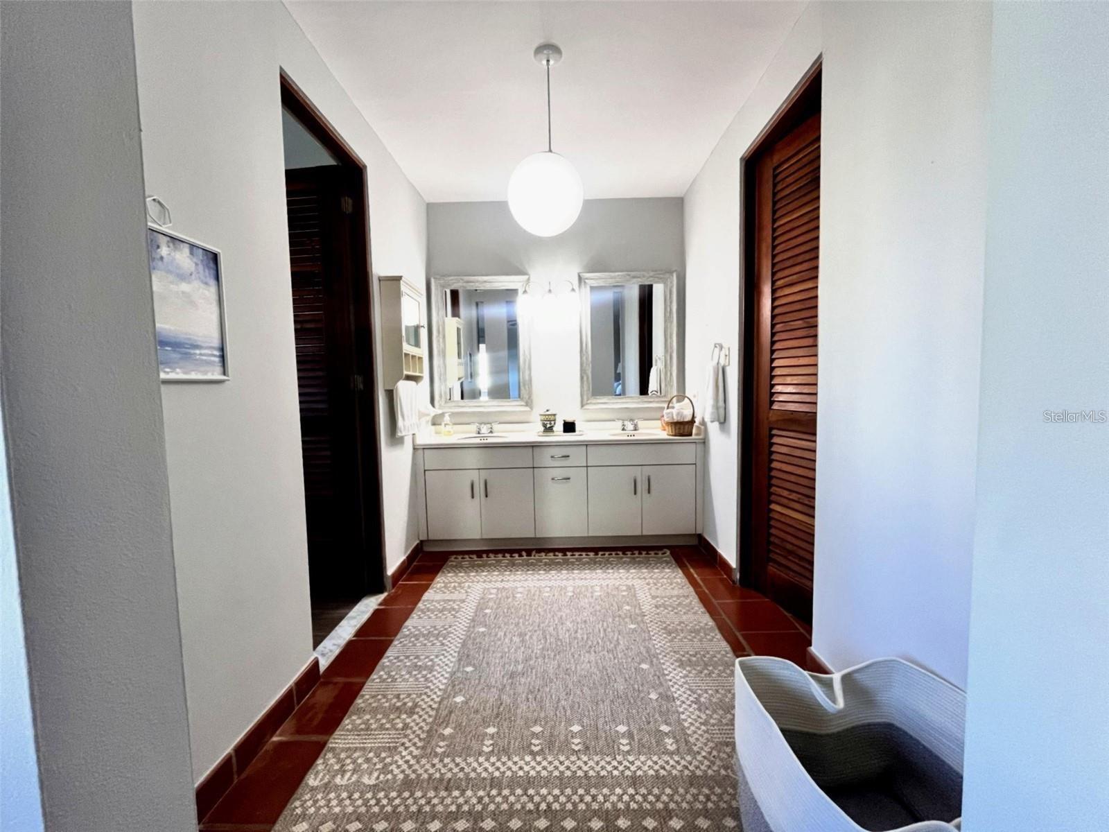 Bathroom vanity with two mirrors, white cabinetry, dark louvered doors, and a patterned runner rug.