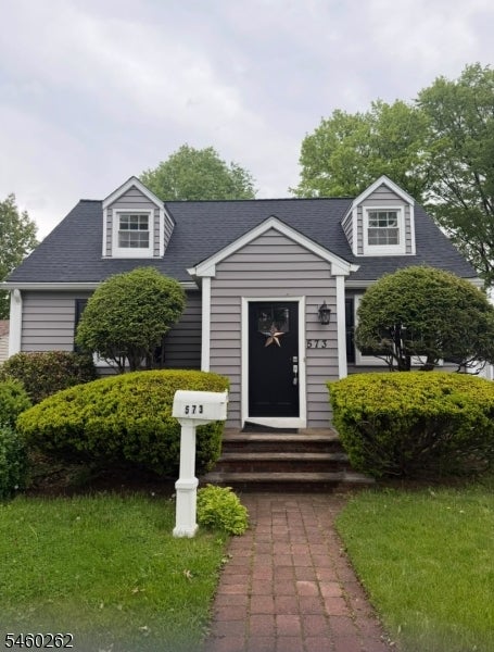 Gray-sided house with dormers, trimmed shrubs, and a brick walkway leading to the front door.