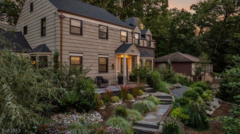 Shingle-sided home with a warmly lit entrance, curved stone garden path, and lush landscaping at dusk.