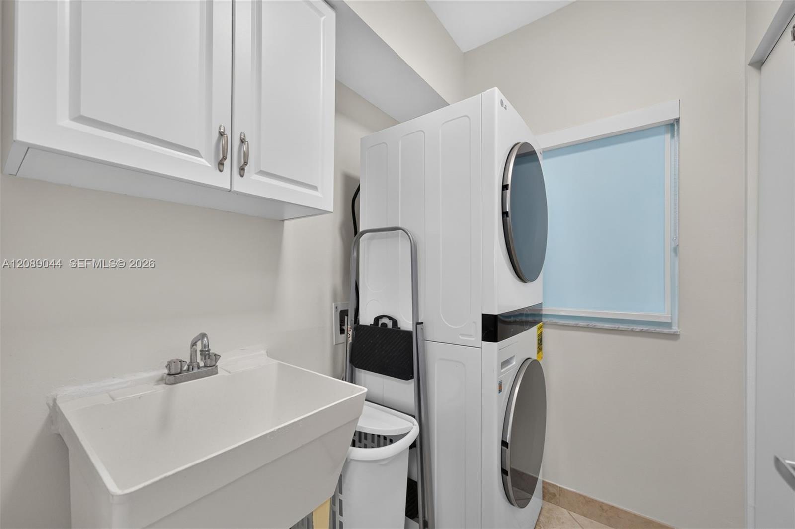 Laundry room with stacked washer and dryer beside a deep utility sink and white cabinets.