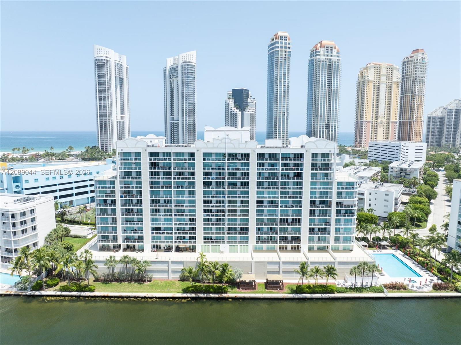 Waterfront condominium with glass balconies, a pool, and oceanfront towers in the background.
