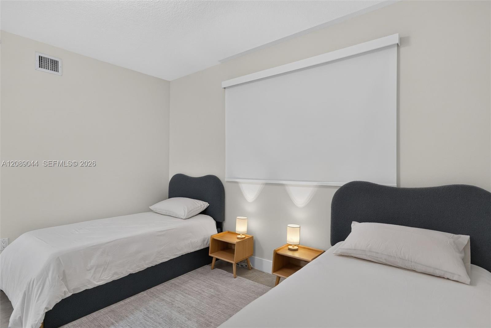 Bedroom with two twin beds, dark upholstered headboards, and wooden nightstands with lamps.