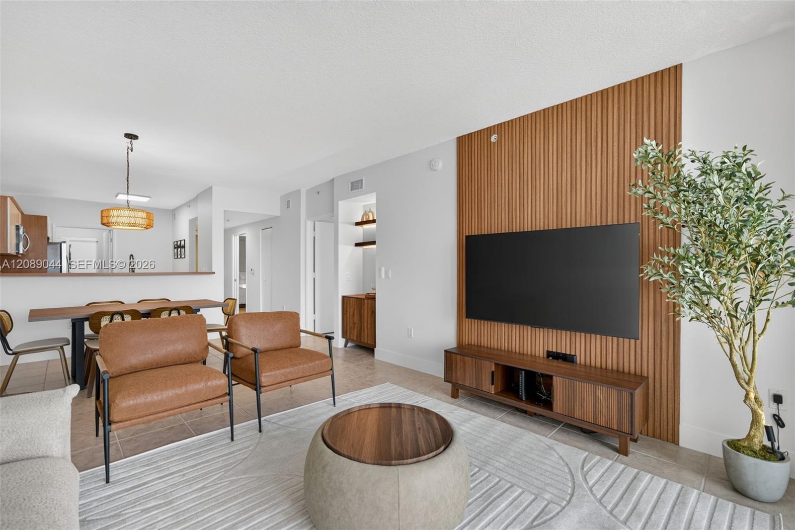 Living and dining area with tan leather chairs and a television on a wood-slat accent wall.