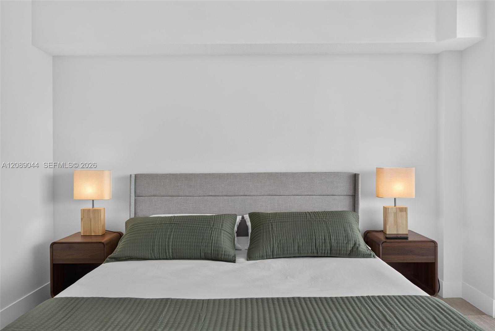 Bedroom with a gray upholstered headboard, green pillows, and matching lamps on wooden nightstands.