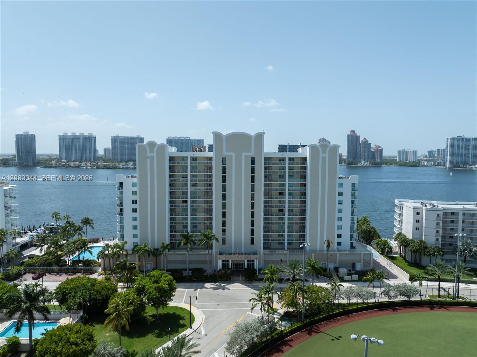 Waterfront condominium tower beside the bay, with a pool and landscaped grounds in front.