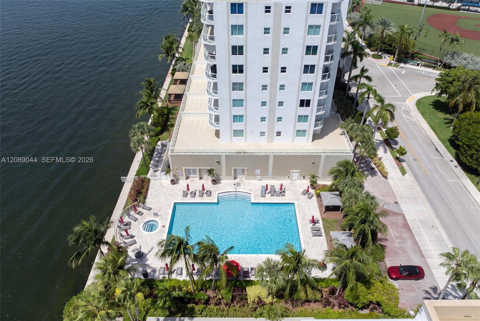 Waterfront condominium with a large pool beside the bay, viewed from above.