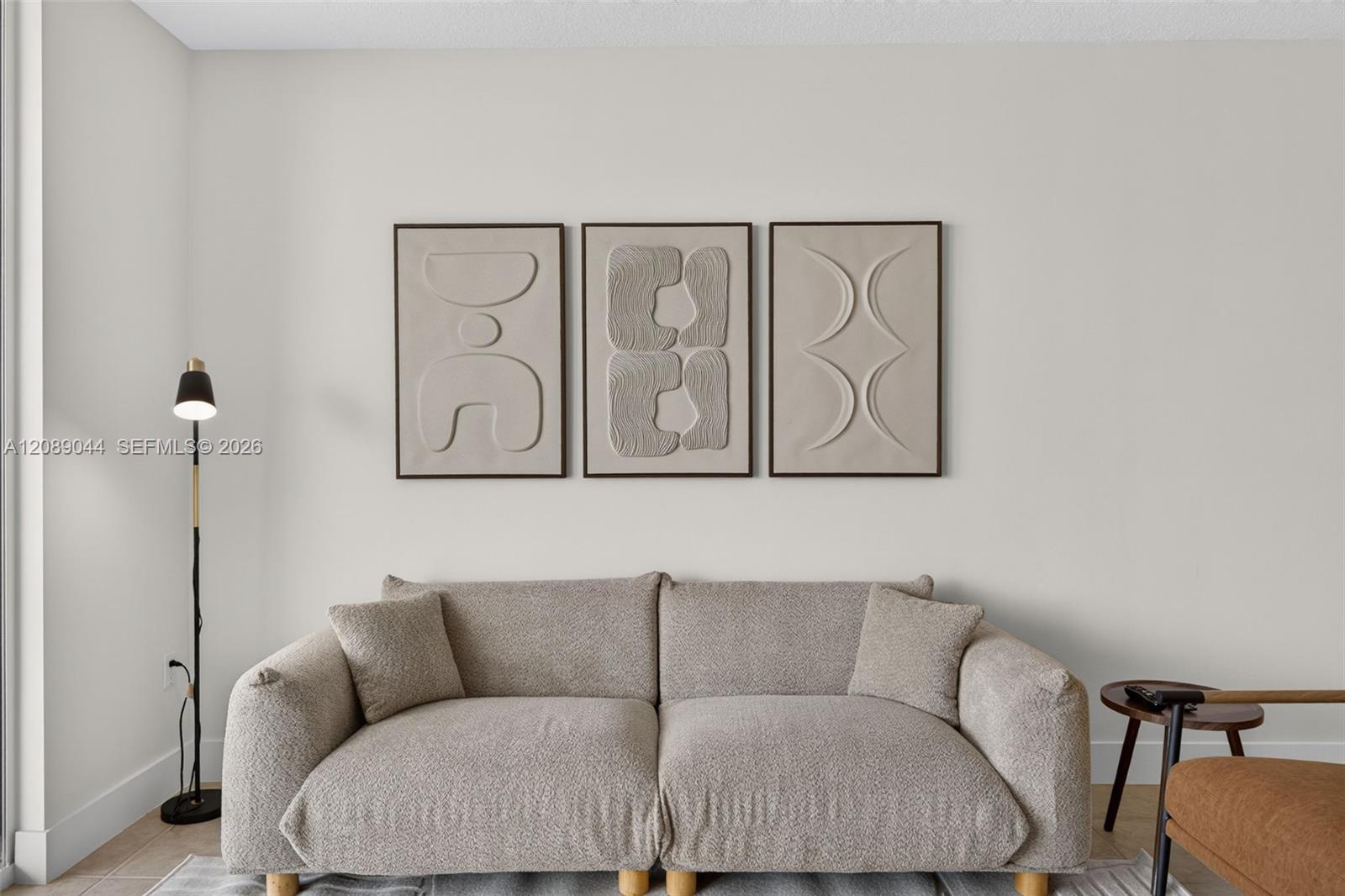 Living room with a curved beige sofa beneath three framed abstract artworks.