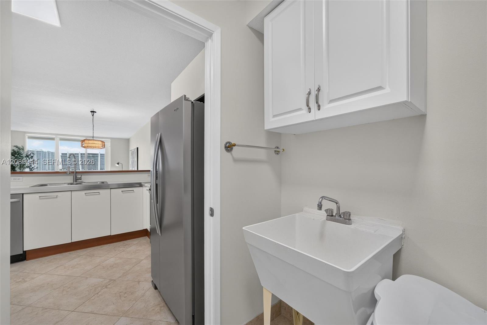 Laundry area with a deep utility sink and stainless-steel refrigerator beside the kitchen.