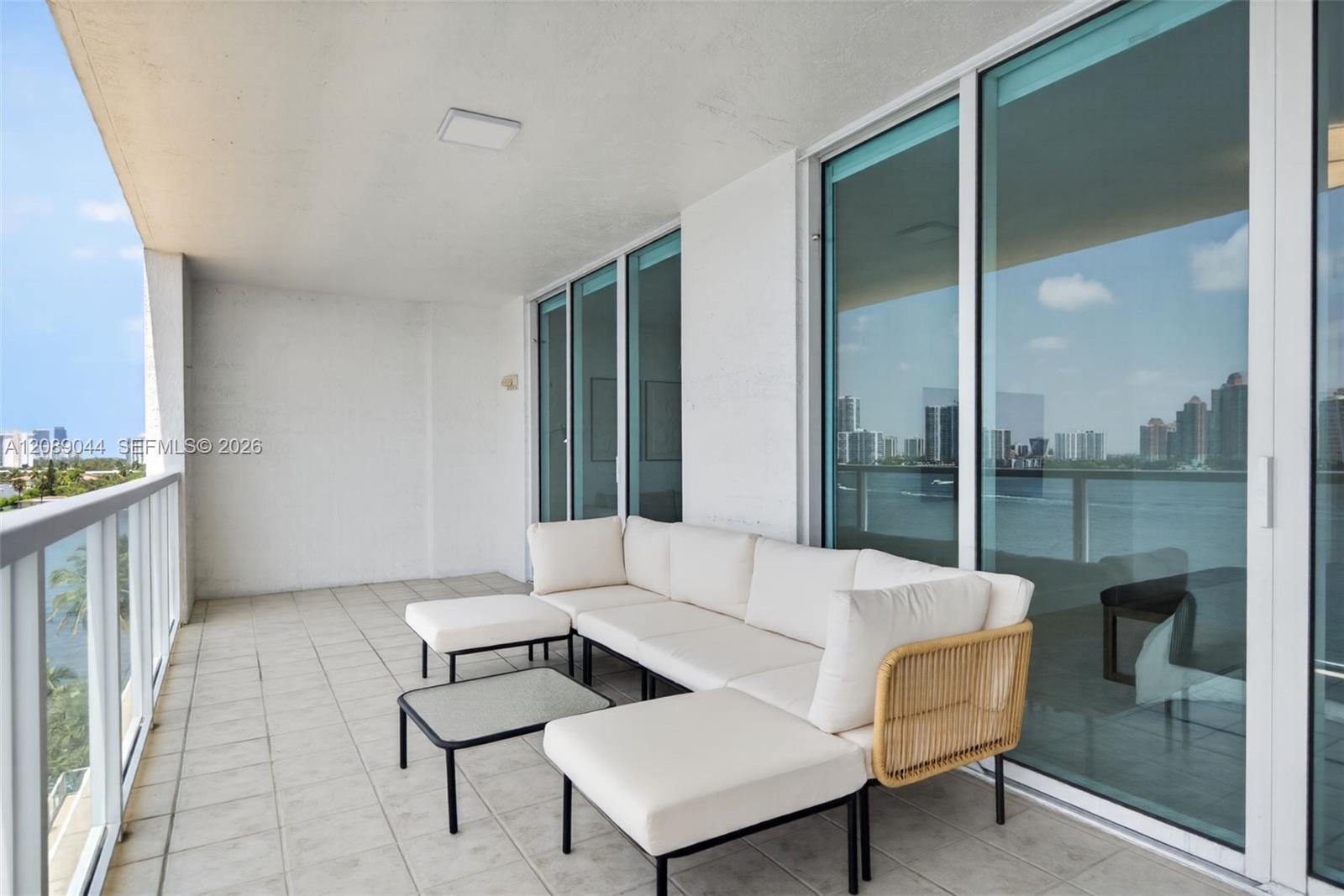 Furnished condo balcony with white sectional seating overlooking the water and city skyline.