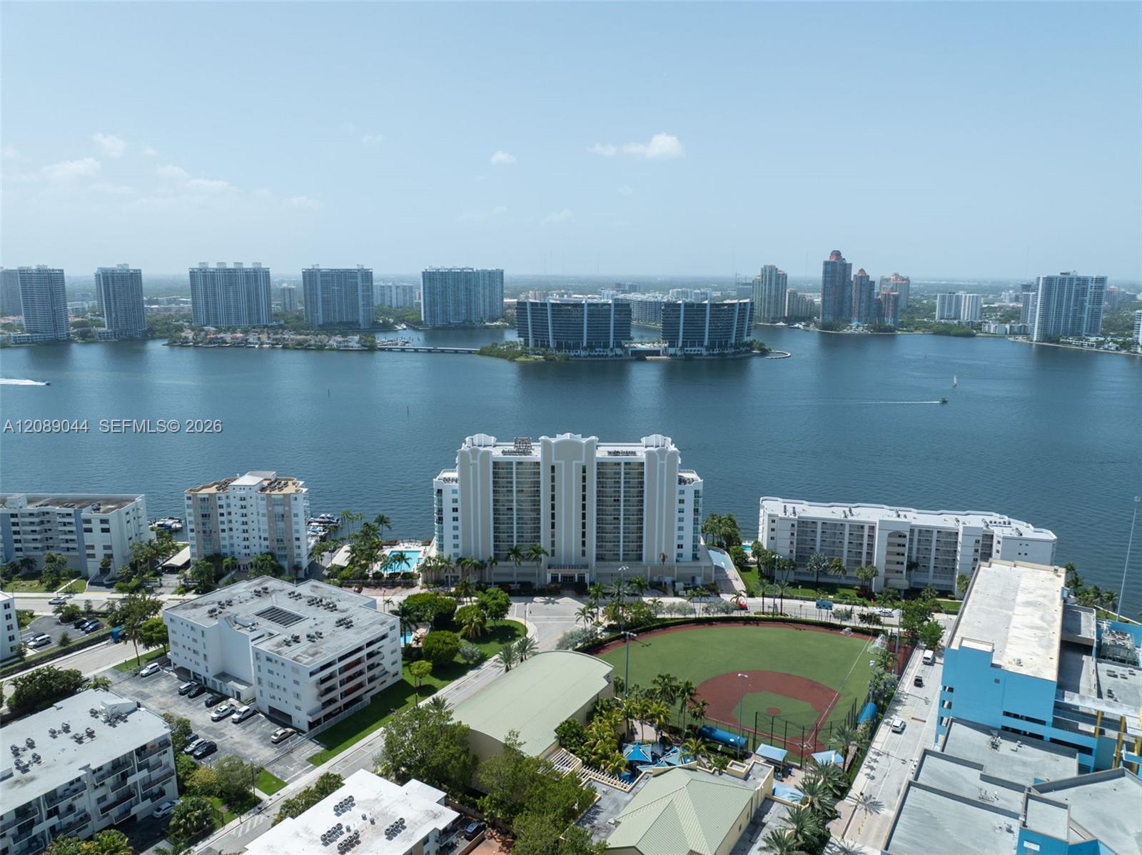 Aerial view across the bay toward waterfront towers, with a baseball field and buildings in the foreground.