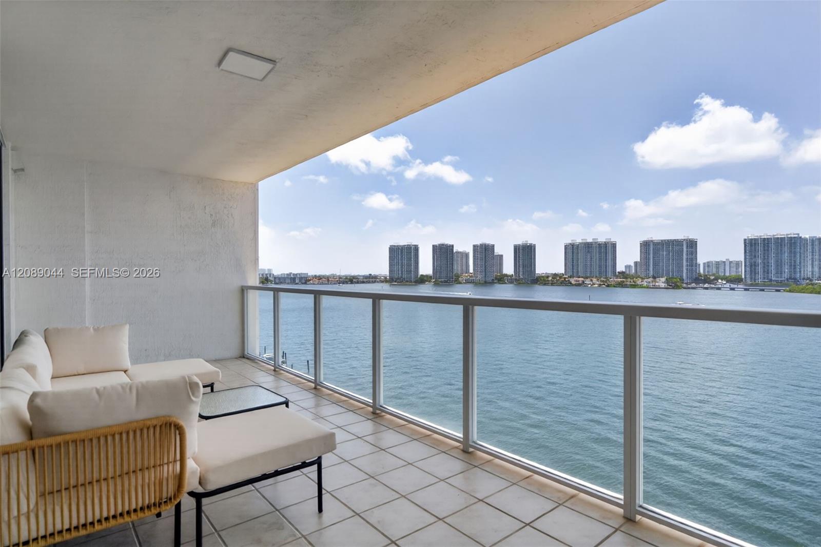 Furnished balcony overlooking the bay, with distant high-rise buildings across the water.