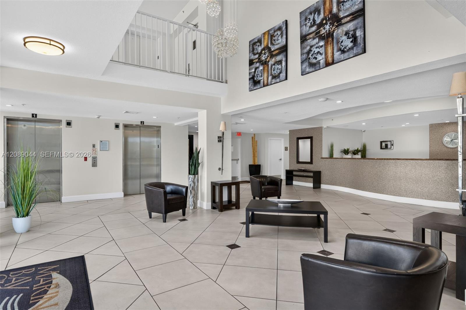 Condominium lobby with two elevators, a reception counter, and seating beneath an open mezzanine.