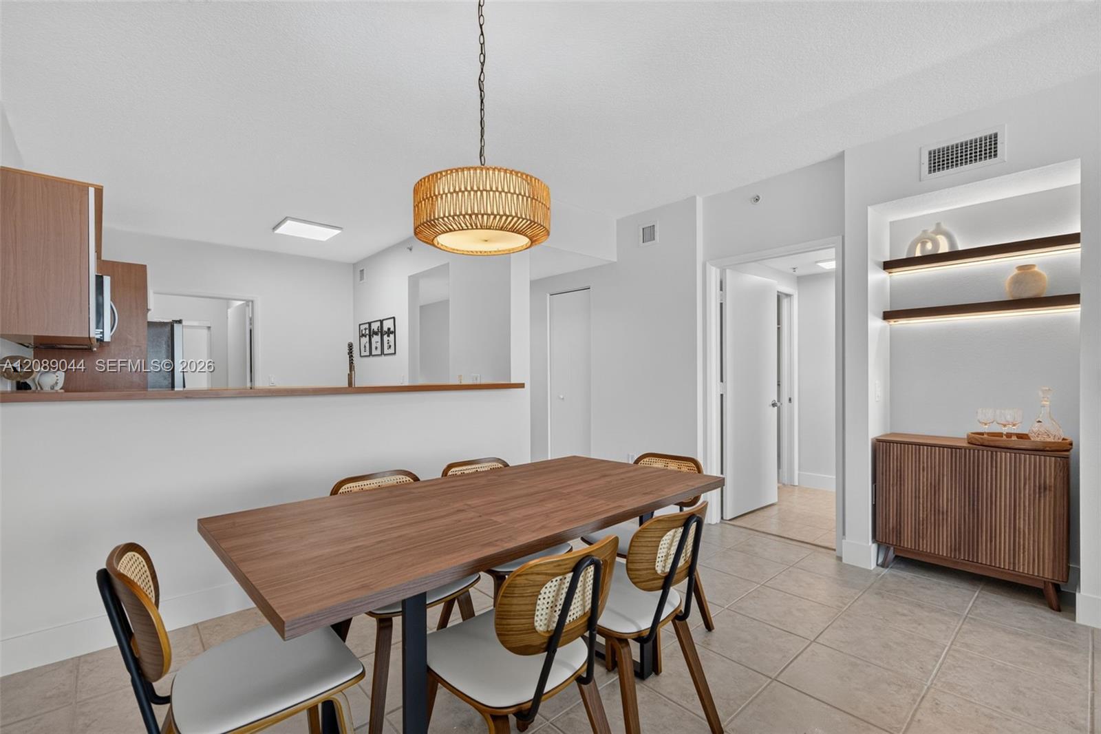 Dining area with a long wood table, woven-back chairs, pendant light, and illuminated display shelves.