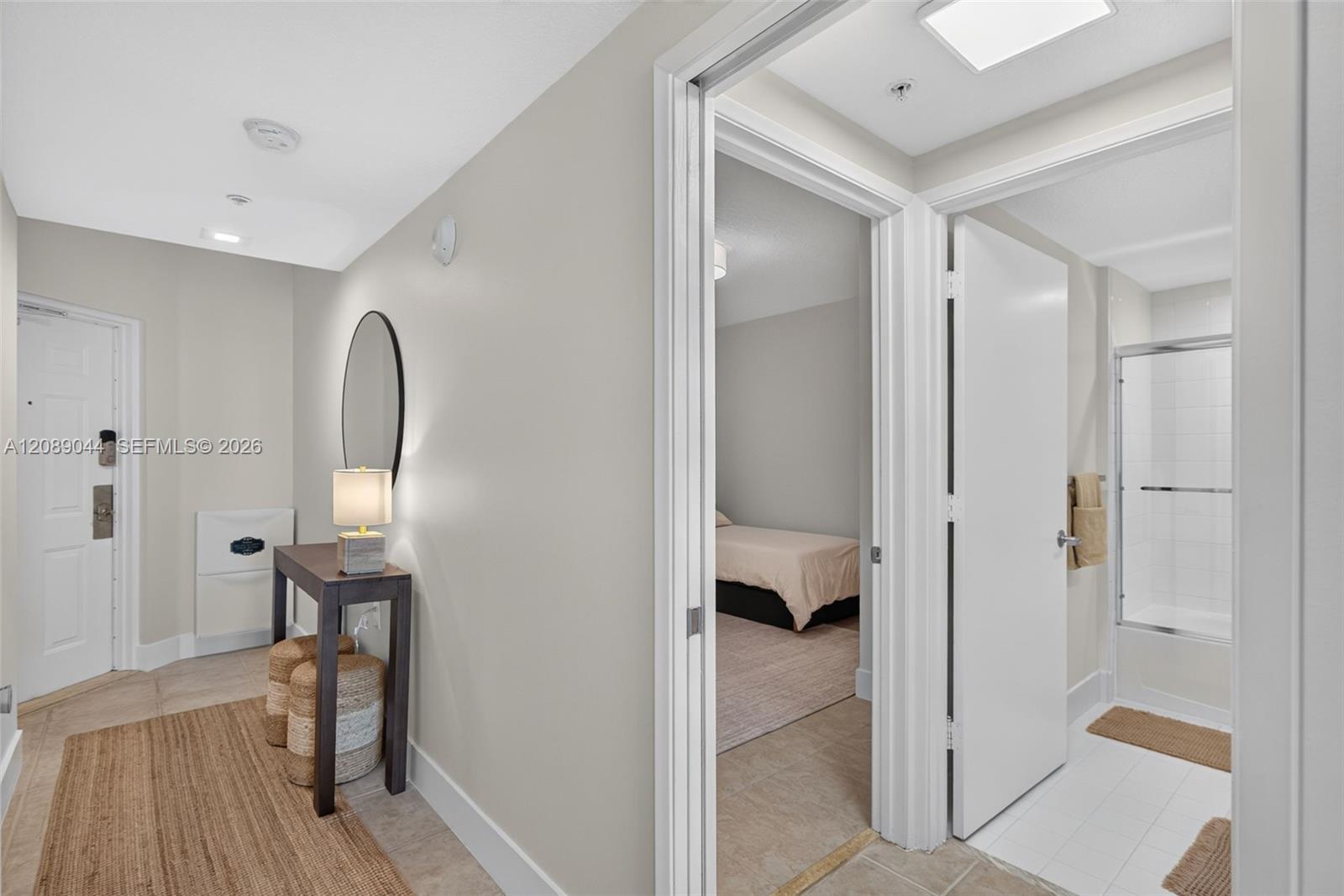 Condo hallway with a console table and woven rug, opening onto a bedroom and bathroom.