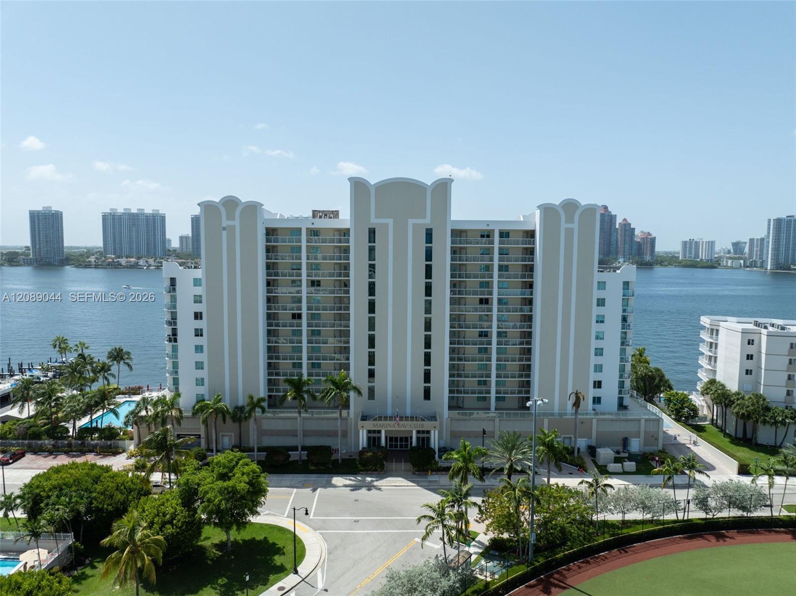 Marina Bay Club condominium beside the water, with a pool, palm trees, and distant high-rises.