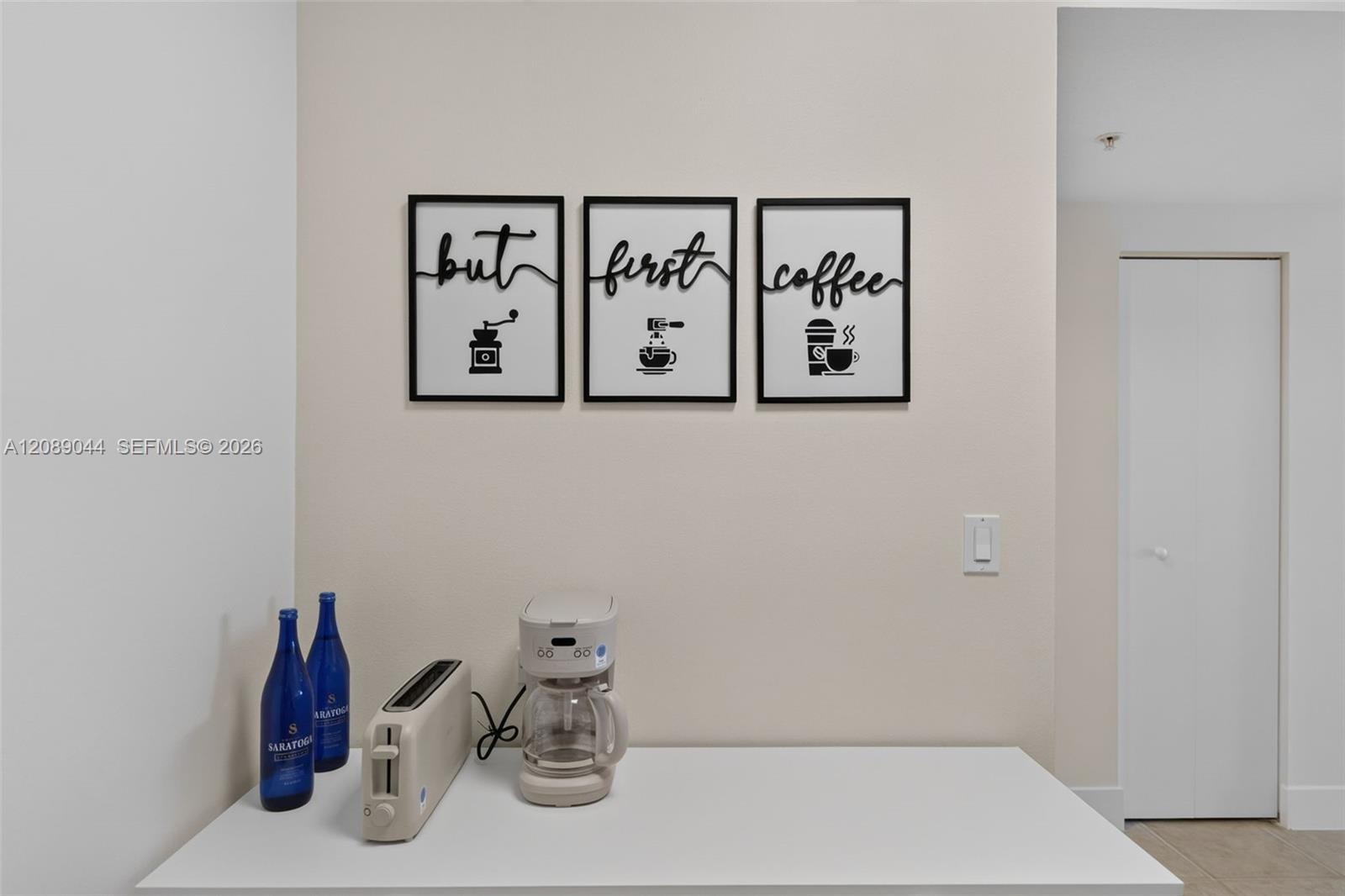 Coffee station with a drip coffee maker, toaster, blue bottles, and framed coffee prints.