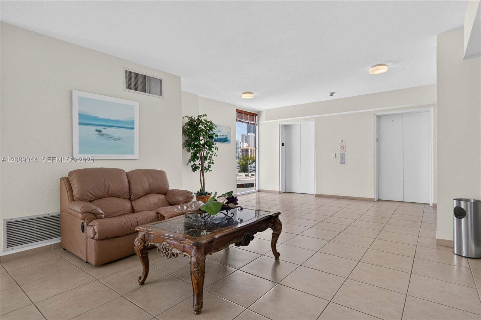 Condominium elevator lobby with a brown leather sofa, ornate coffee table, tiled floors, and a view of nearby buildings.