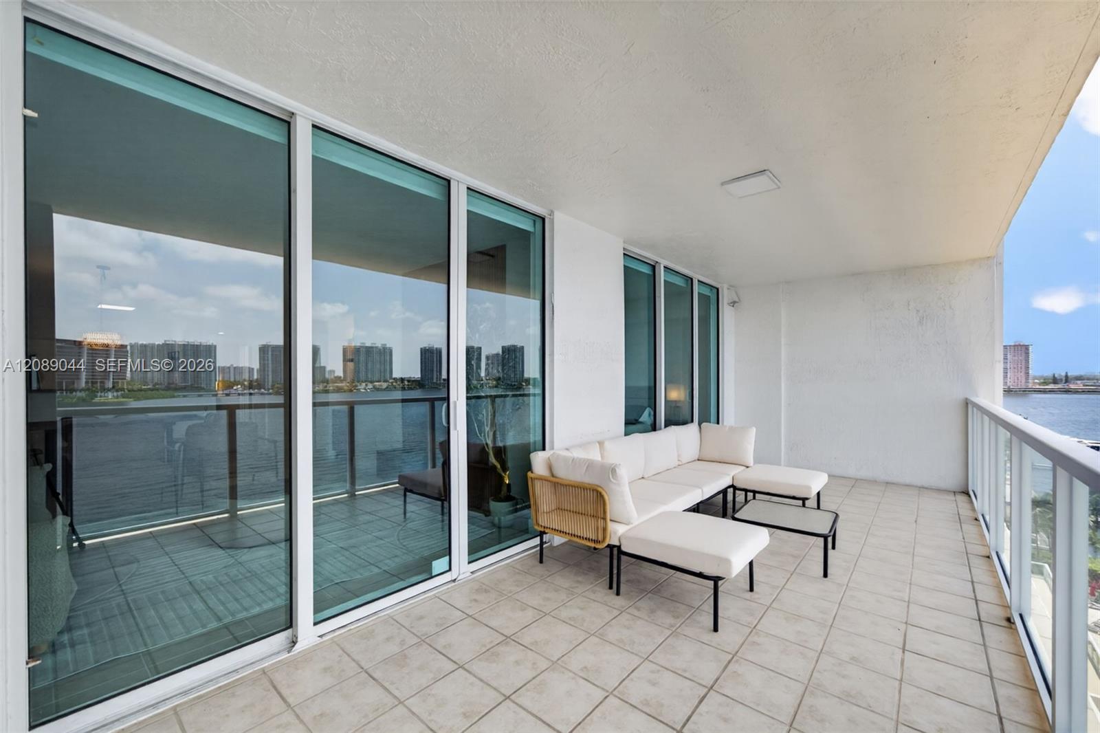 Furnished balcony with white lounge seating and views over the water toward the skyline.