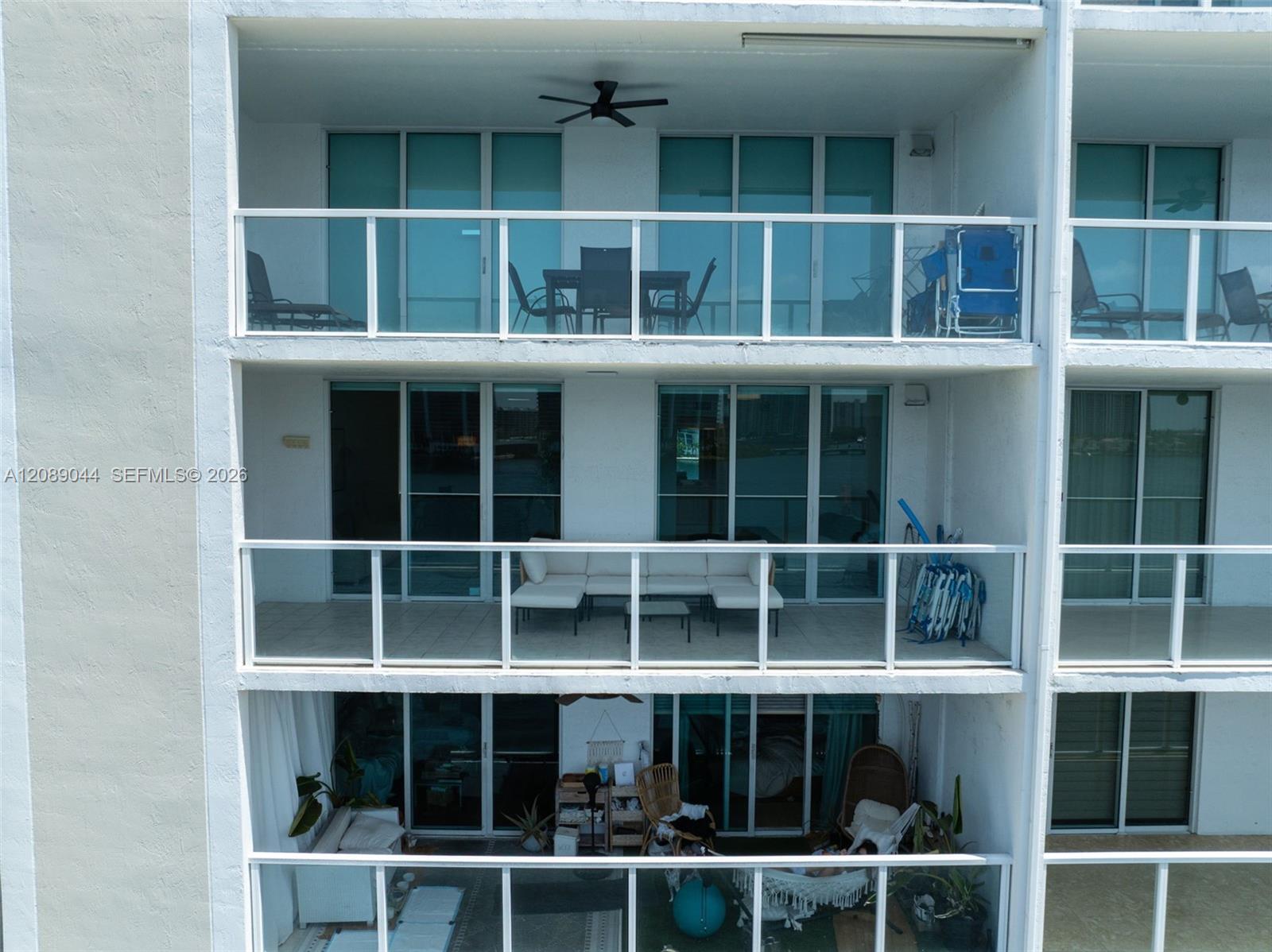 Condominium exterior with stacked glass-railed balconies, patio furniture, and water visible through the windows.