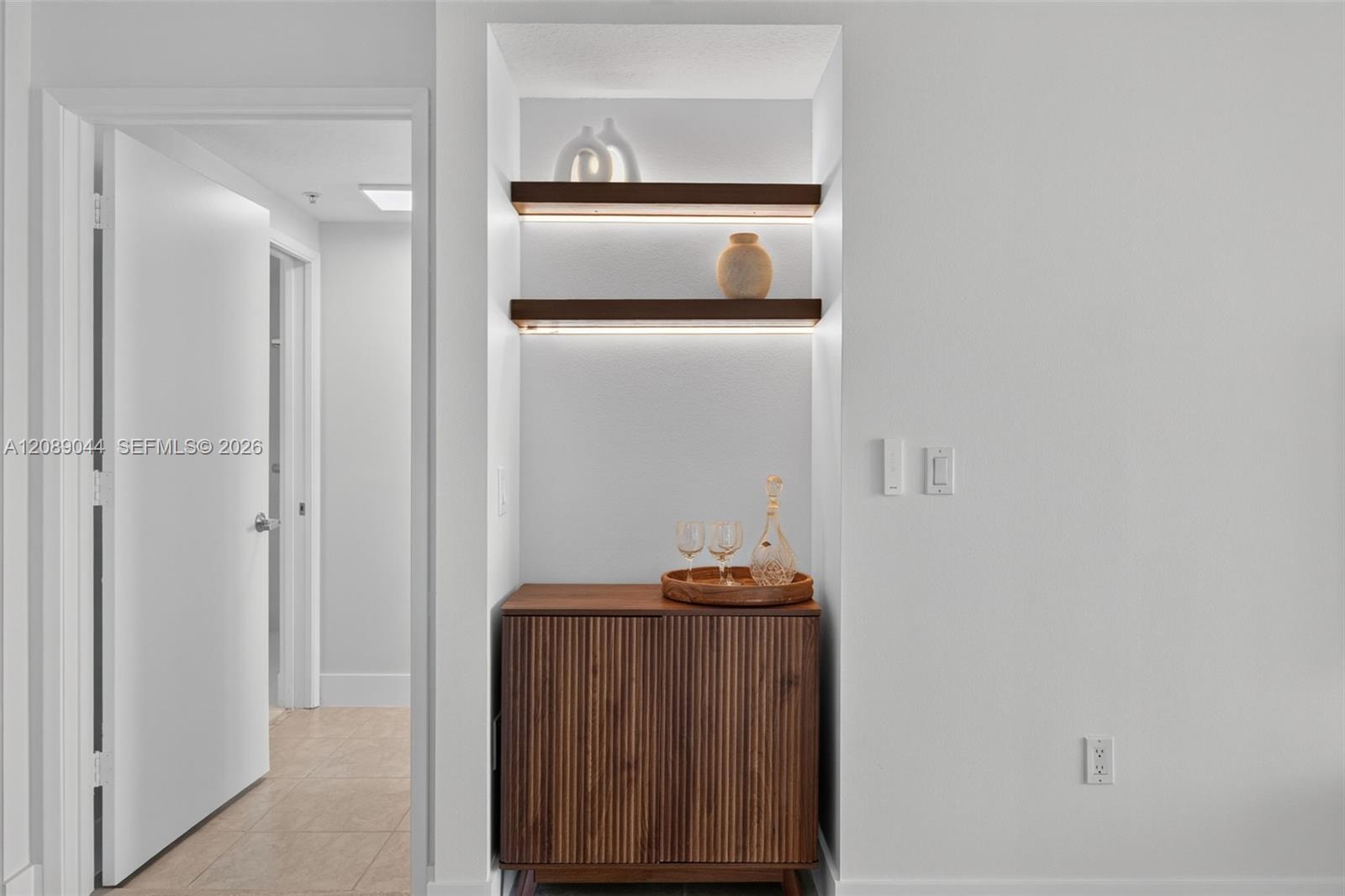 Apartment entryway with a fluted wood console and illuminated display shelves.