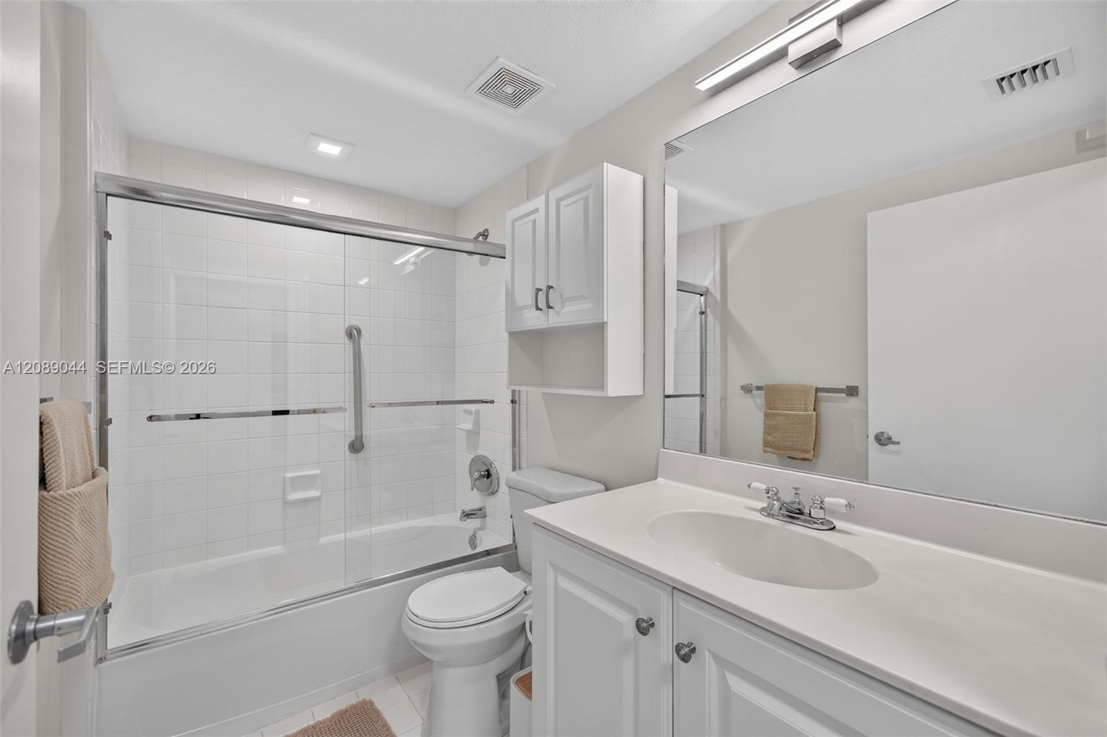 White bathroom with a glass-enclosed tub and shower, grab bars, toilet, and vanity.