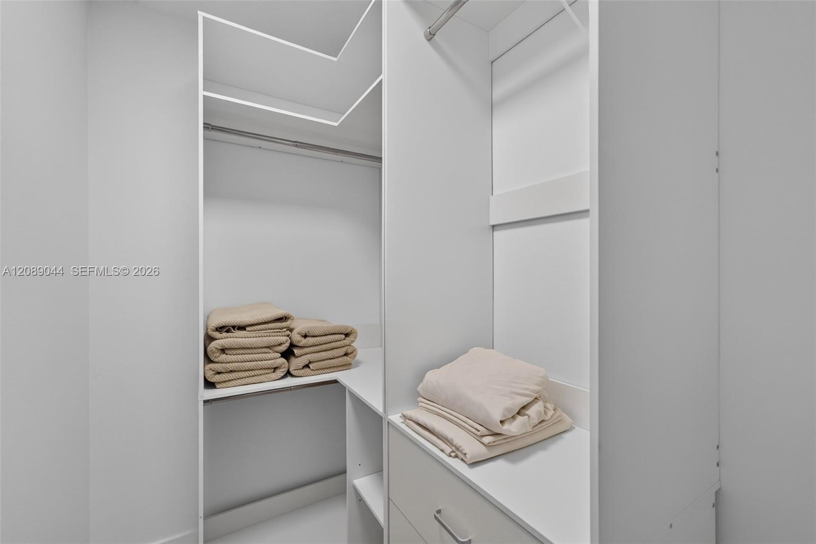 Walk-in closet with white built-ins and neatly folded beige towels.