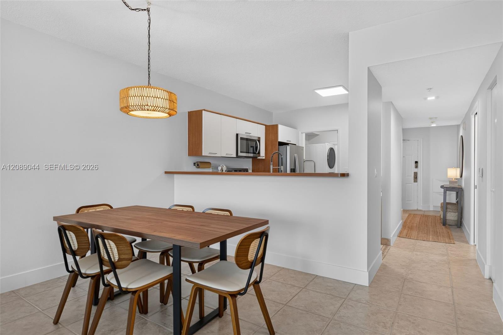 Dining area with a wood table and woven pendant beside an open kitchen.