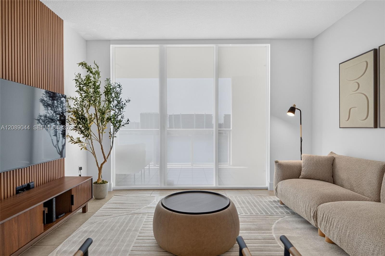 Living room with a beige sectional, round coffee table, and wood-slat TV wall beside sliding balcony doors.