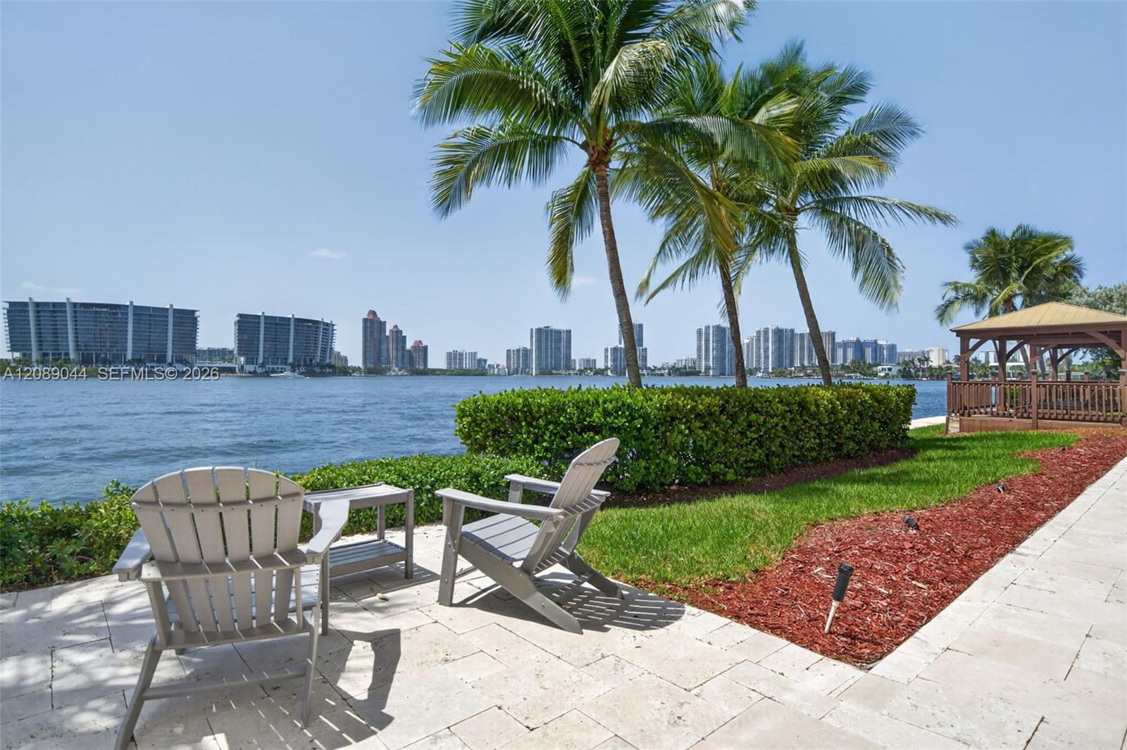 Waterfront patio with lounge chairs, palm trees, and a bay view toward the distant skyline.